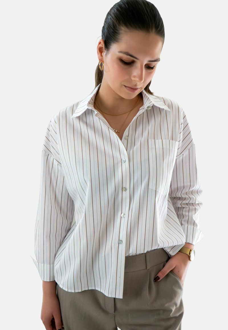 Witte button-up blouse met verticale strepen in lichtbruin, voorzien van een zak, puntkraag en lange mouwen, gecombineerd met beige broek.