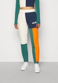 Housut värilohkoilla, joissa on osiot tummansinisestä, kermasta, tealiin ja oranssista, elastisella vyötäröllä ja logotiedolla reisissä.