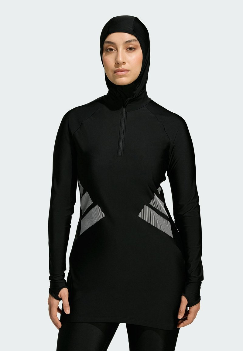 Sort atletisk tunika med høj hals og lynlås, med teksturerede grå diagonale detaljer på siderne. Lange ærmer med hul til tommelfingrene.