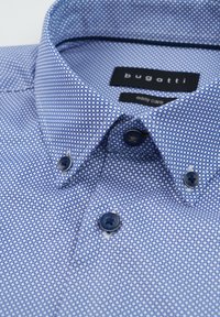 Blaue gemusterte Hemd mit Kragen, das ein gepunktetes Design in hellblau aufweist. Enthält dunkelblaue Knöpfe und ein "Bugatti"-Etikett im Kragen.
