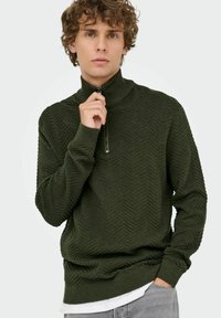 Dunkelgrüner Strickpullover mit hohem Kragen, zigzagförmiger Textur, langen Ärmeln und einem halben Reißverschluss.