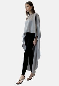 Silverfärgad lång topp i satin med flödande, asymmetrisk fåll, bärs över svarta leggings och kombineras med svarta remklackar. Mjuk textur; elegant design.