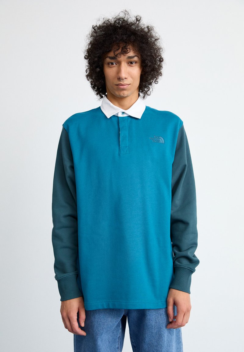Turquoise langoordig polo met een witte kraag, voorzien van een donkergroene mouw en logo op de borst, gemaakt van een zachte katoenmix.