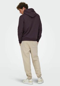 Haut à capuche violet foncé avec une poche kangourou, associé à un pantalon de survêtement beige et des baskets blanches avec des accents clairs.