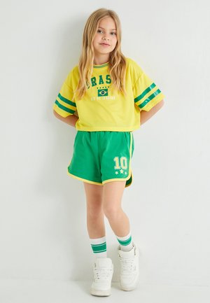 Camiseta corta amarilla con rayas verdes y texto "BRAZIL"; pantalones cortos verdes con ribete blanco y impresión de "10"; zapatillas altas blancas.