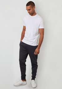 Vit bomullst-shirt kombinerad med mörkgrå joggers. Joggers har elastiska muddar och sidofickor, kompletterade med vita sneakers.