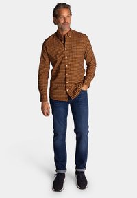 Geruit oranje en zwarte button-up shirt met een kraag, gecombineerd met blauwe jeans en donkere sneakers. Heeft lange mouwen en een ontspannen pasvorm.