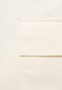 Tissu en coton beige avec une poche rectangulaire cousue. La texture est lisse et les bords sont soigneusement finis sans matérielles visibles.