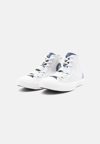 Ζευγάρι λευκών ψηλών αθλητικών παπουτσιών με μπλε λεπτομέρειες και λευκές κορδόνες, τοποθετημένα το ένα δίπλα στο άλλο σε απλό φόντο.