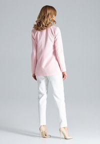 Blazer in lichtroze stof met lange mouwen, gecombineerd met witte op maat gemaakte broek en naaktsandalen met hoge hakken, bekeken vanuit de achterkant.
