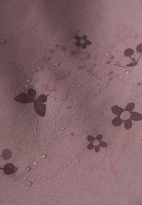 Gouttes d'eau sur un tissu mauve avec des motifs de papillons et de fleurs violet foncé.