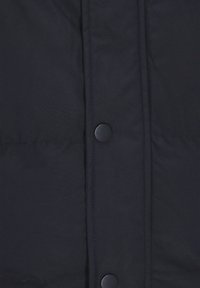 Marineblå pufferjakke med en glat tekstur, der har store quiltede sektioner og sorte trykknapper langs fronten til lukning.