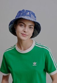 Blue denim bucket hat with frayed edges, paired with a green t-shirt featuring white trim and three white stripes on the sleeves.