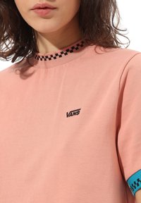 Różowa koszulka z krótkim rękawem, z okrągłym czarnym kołnierzykiem w szachownicę oraz turkusowym akcentem na rękawie, z małym czarnym logo Vans.