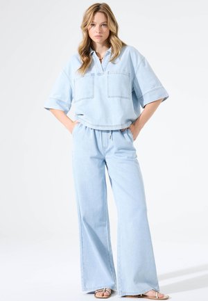 Conjunto de mezclilla azul claro que incluye un top de manga corta con cuello y dos bolsillos, junto con pantalones de pierna ancha. Textura suave y ajuste relajado.