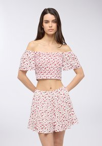 Crop top off-the-shoulder e gonna abbinata, entrambi bianchi con stampa floreale rossa. Presenta un design arricciato e una gonna a più strati con orlo arricciato.
