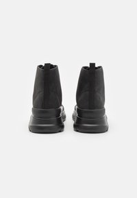 Černé kotníkové boty se svrchním dílem z semiše a texturovanou gumovou podrážkou. Mají poutko pro snadné nazouvání a elegantní, minimalistický design.