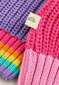 Bunte gestrickte Accessoires mit lila, rosa und mehrfarbigen Streifen. Enthält ein kleines Stoffetikett mit einem Regenbogendesign.