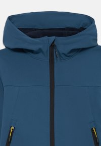 Veste à capuche en tissu bleu foncé avec une fermeture éclair à l'avant, deux poches latérales avec des zips noirs et des accents jaunes contrastants.