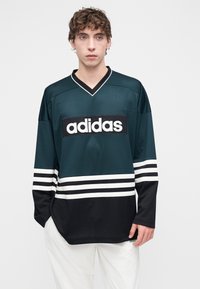 Türkizkék és fekete hálós mez fehér csíkokkal, feltűnő fekete "adidas" logóval. V-nyakú kialakítás, laza szabás, hosszú ujjú.