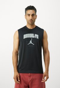 Svart ermeløs skjorte laget av glatt stoff har teksten "BROOKLYN" og et Jumpman-logo i grått, med en avslappet passform og rund hals.
