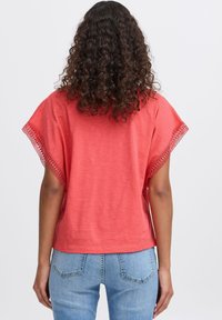 Koralfarvet bomuldsbluse med brede ærmer og blonder i kanterne, parret med lyseblå denimjeans. Enkel, afslappet pasform.