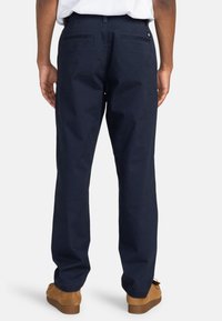 Navy blue cotton trousers with a straight-leg design, featuring two back pockets, and a button closure at the waist. Smooth texture.