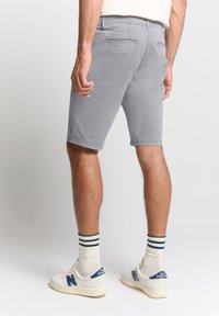 Grijze shorts van een gladde stof, tot de knie, met achterzakken. Gecombineerd met witte sneakers en gestreepte sokken.