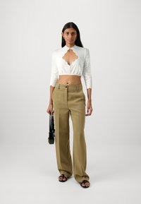 Biely čipkový crop top s klobúkovým výstrihom, kombinovaný s béžovými nohavicami s vysokým pásom. Čierna kabelka a ploché sandále dotvárajú vzhľad.
