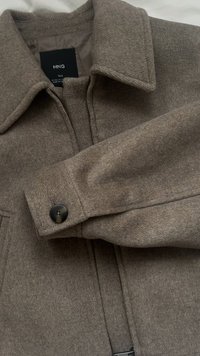 Wool jacket in light brown with a flat collar, zip closure, and black button details on the cuffs. Soft texture, tailored design.