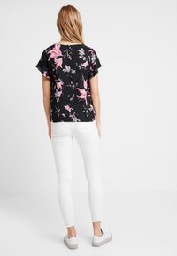 Černá květinová blůza s krátkým rukávem, zdobená růžovými a bílými vzory. V kombinaci s bílými skinny džínami a volnočasovými teniskami.
