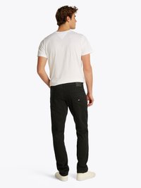 Fekete farmernadrág slim fit szabással, fehér, rövid ujjú pamut pólóval párosítva. A farmernadrág hátsó zsebekkel és diszkrét logózással rendelkezik.