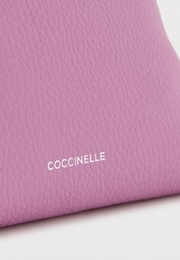 Paarse leren handtas met een gestructureerd oppervlak en een in reliëf aangebracht merklogo "Coccinelle" in wit.