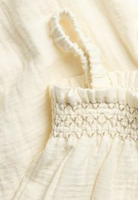 Crème-kleurige jurk met een gesmokt lijfje met gerimpelde randen en dunne, gathered schouderbanden. Zachte textuur met een lichtgewicht, vloeiende ontwerp.
