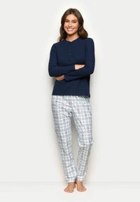 Marineblå langærmet top med knaplukning, parret med hvide rutede bukser med orange accenter og små blomster mønstre.