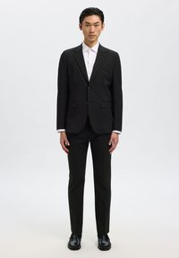 Czarny garnitur o dopasowanym kroju, jednorzędowy fason, dwie przednie kieszenie oraz biała koszula pod spodem. Gładka faktura tkaniny.