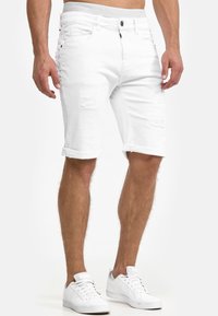 Witte denim shorts met opgerolde cuffs, met verouderde details. Gepaard met witte sneakers, wat zorgt voor een casual, moderne uitstraling.