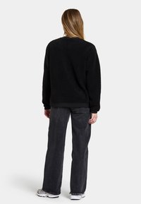 Maglione in pile nero e morbido con scollatura rotonda, spalle scese e polsini a costine, abbinato a jeans grigi scuri a vita alta e sneakers bianche.