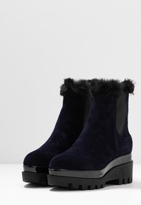 Granatowe zamszowe botki za kostkę z futrzanym kołnierzem, elastycznymi panelami po bokach i masywnymi czarnymi platformami z teksturowanym wzorem na podeszwie.