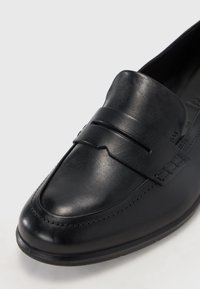 Black leather loafer with a rounded toe, featuring a raised band across the instep and subtle stitching details along the edges.