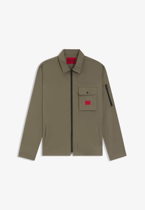 Giacca leggera verde oliva con colletto, zip frontale e tasca sul petto con etichetta rossa del marchio. Include tasche laterali e dettagli con zip.