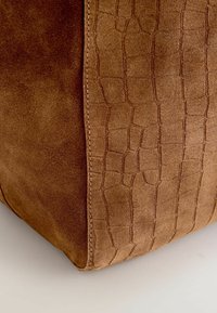 Braune Wildledertasche mit strukturiertem Krokodil-Muster auf einer Seite, die sauber genähten Nähte entlang der Naht für zusätzliche Details aufweist.