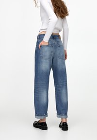 Světle modré, vysoké džíny s volným střihem, ohrnuté lemy a dvě zadní kapsy; mají hnědou koženou visačku na pase.