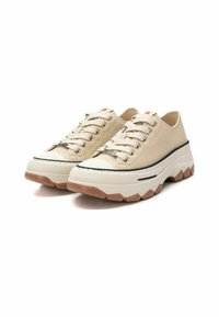 Zapatillas de lona beige con suela gruesa blanca y marrón claro, detalle de raya negra y cordones planos. Punta redondeada y lengüeta acolchada.