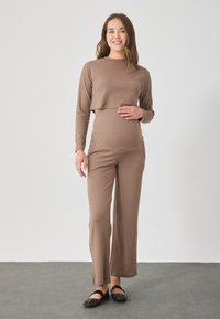 Hnedý rebrovaný crop top a zodpovedajúce vysoké nohavice, vyrobené z mäkkého materiálu, skombinované s čiernymi balerínkami. Oblečenie je navrhnuté pre pohodlie.