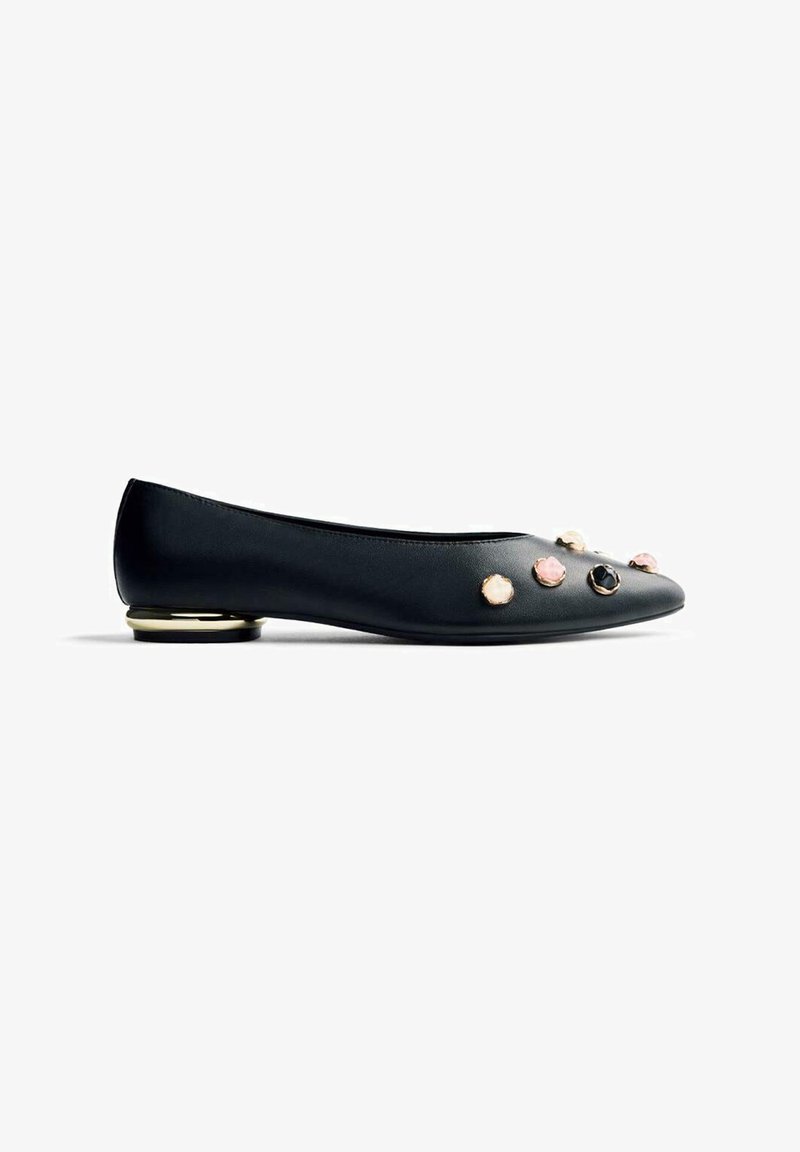 Ballerines en cuir noir avec un bout pointu, ornées de bijoux décoratifs et d'une touche dorée au talon. Texture lisse et design minimal.