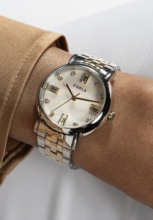 Orologio Furla con cinturino metallico rotondo in argento e oro, quadrante in madreperla bianca e indici delle ore rettangolari. Presenta una corona a pressione.