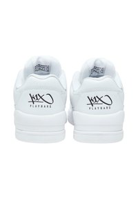 White sneakers with smooth leather and mesh accents. Features rounded heel, flat sole, and black "K1X PLAYHARD" logo on the back.