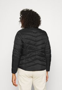Schwarze Steppjacke mit Chevron-Muster, hohem Kragen und langen Ärmeln. Glatte Textur mit genähten Bereichen, stilisiert für Isolierung.