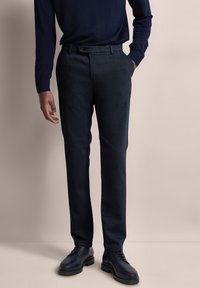 Aangepaste donkerblauwe pantalon in een gestructureerde stof met een rechte pijp, voorzien van vo pockets en een contrasterende knoopsluiting.